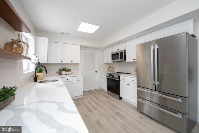 kitchen featuring visible vents, light stone countertops, white cabinets, stainless steel appliances, and a sink