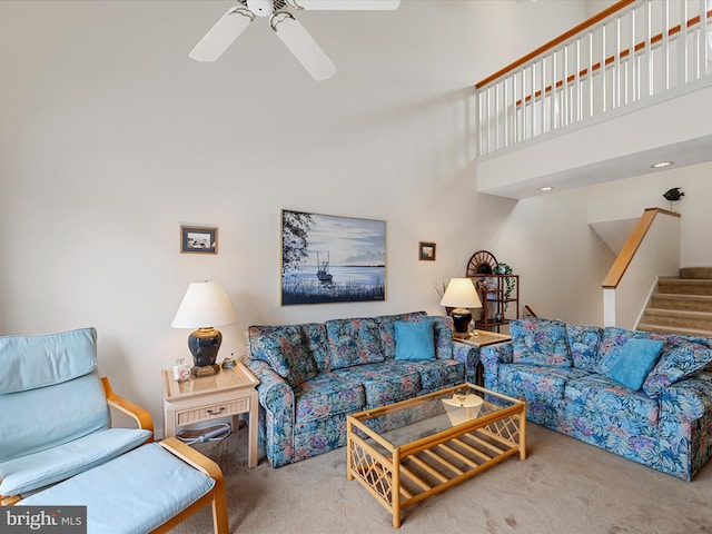 living room with a towering ceiling, stairs, a ceiling fan, and carpet floors