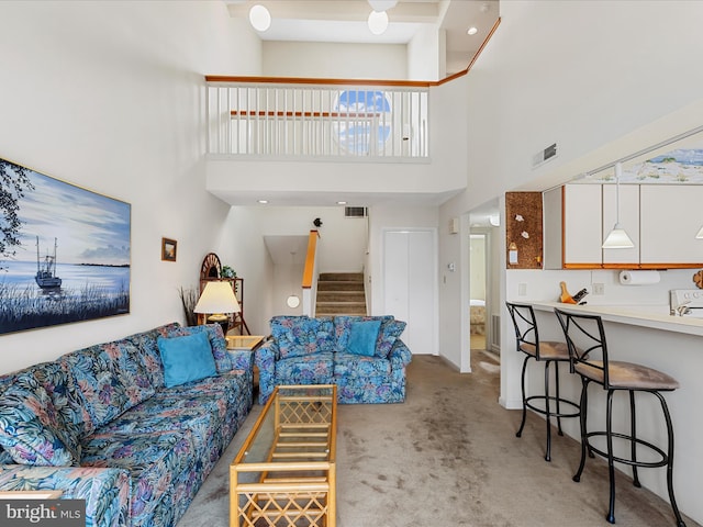 living area featuring light carpet, visible vents, stairs, and a towering ceiling