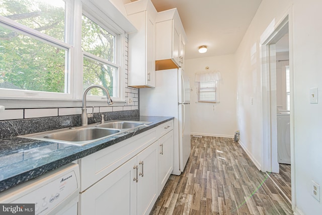 kitchen with washer / clothes dryer, wood finished floors, white dishwasher, white cabinetry, and a sink