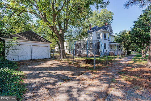 view of front of property with an outbuilding, a garage, fence, a trampoline, and a chimney