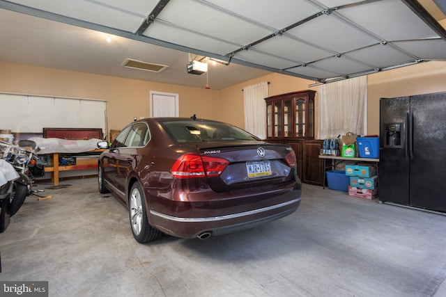 garage with a garage door opener and black fridge with ice dispenser