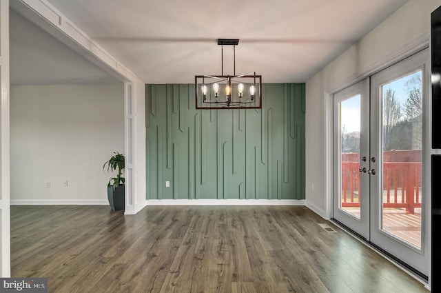 unfurnished dining area with a notable chandelier, wood finished floors, visible vents, baseboards, and french doors