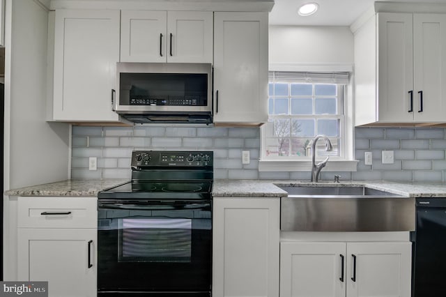 kitchen featuring white cabinets, decorative backsplash, light stone countertops, black appliances, and a sink