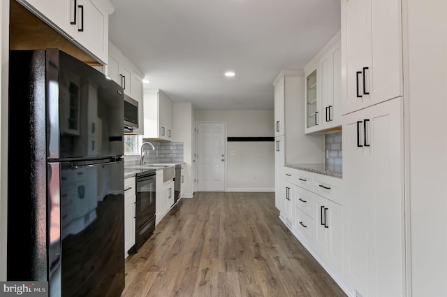 kitchen featuring glass insert cabinets, white cabinets, black appliances, and wood finished floors