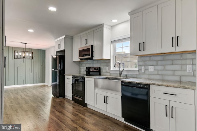 kitchen featuring light stone counters, dark wood-type flooring, a sink, black appliances, and tasteful backsplash