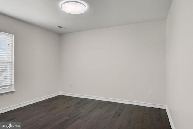 unfurnished room with dark wood-type flooring, visible vents, and baseboards