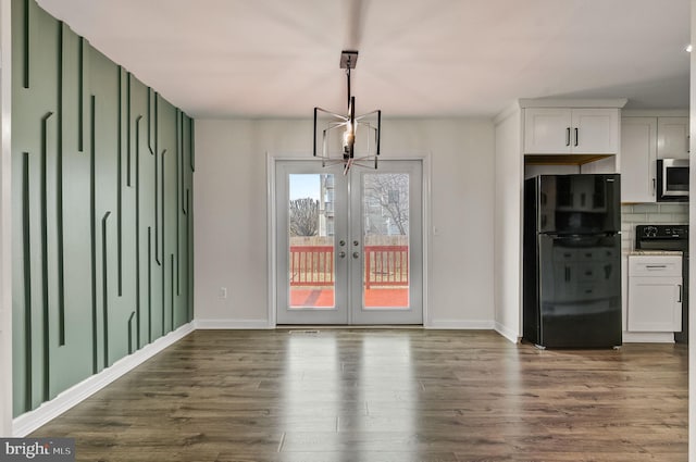 unfurnished dining area featuring french doors, dark wood finished floors, baseboards, and an inviting chandelier