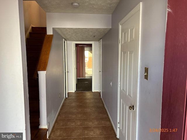 corridor with dark tile patterned floors, a textured ceiling, baseboards, and stairs