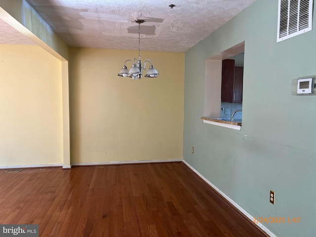 unfurnished dining area with a chandelier, a textured ceiling, wood finished floors, visible vents, and baseboards