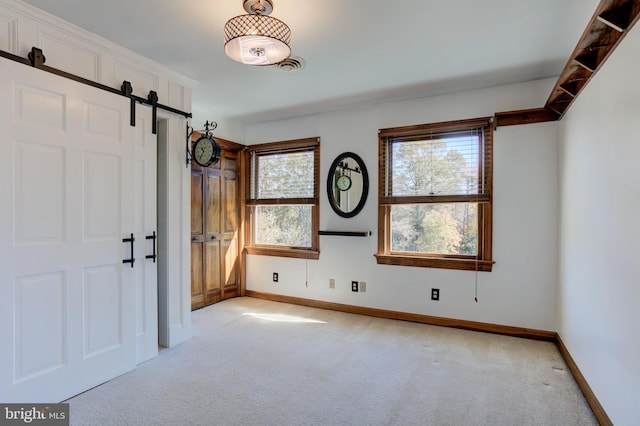 interior space featuring light colored carpet, baseboards, and a barn door