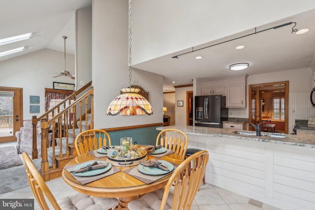 dining space featuring a skylight, light tile patterned floors, ceiling fan, stairs, and high vaulted ceiling