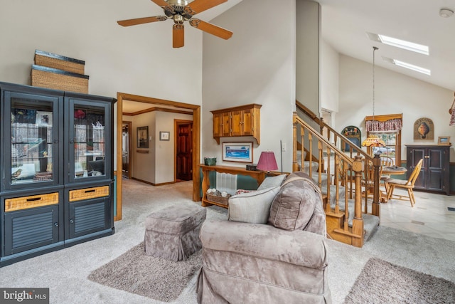 living room with a skylight, a ceiling fan, light carpet, high vaulted ceiling, and stairs