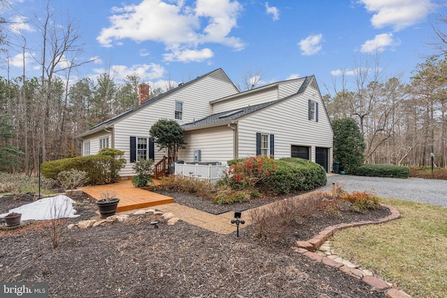 view of side of home featuring a garage, a chimney, driveway, and a deck