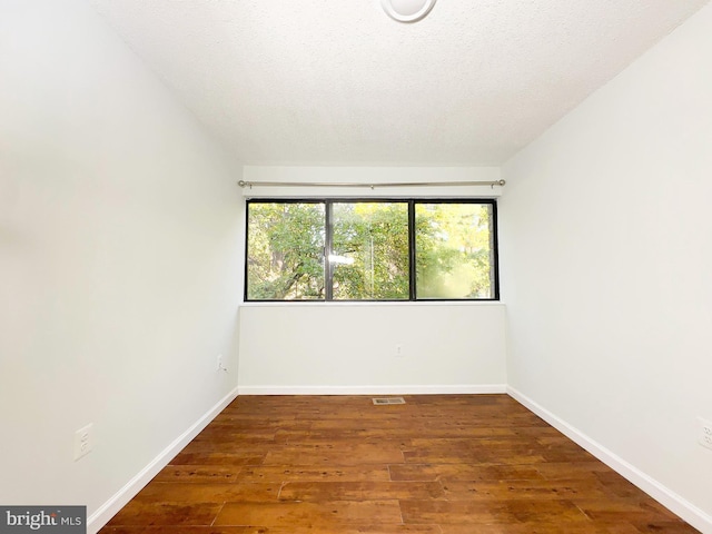 unfurnished room with a textured ceiling, wood finished floors, visible vents, and baseboards