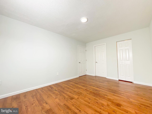 unfurnished bedroom featuring light wood finished floors, baseboards, and a textured ceiling