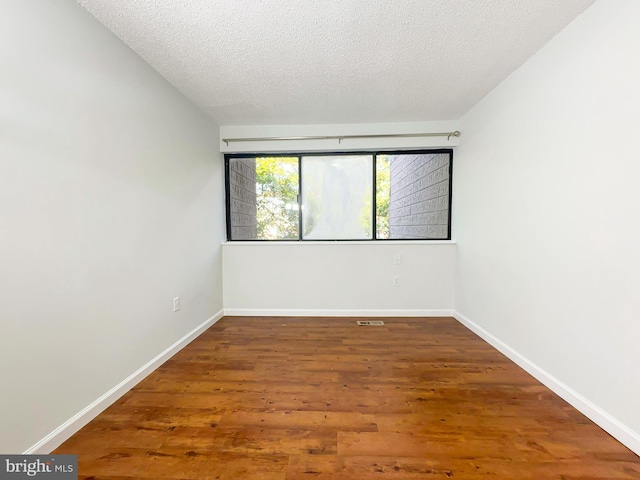 empty room featuring a textured ceiling, baseboards, and wood finished floors