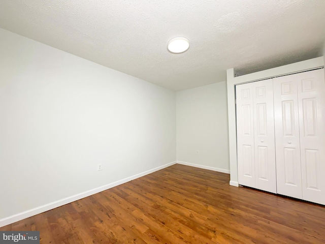 unfurnished bedroom featuring a textured ceiling, a closet, baseboards, and wood finished floors