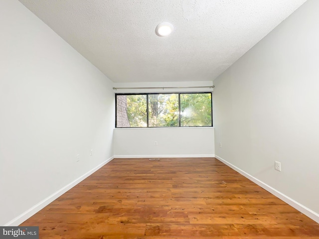 unfurnished room with a textured ceiling, baseboards, and wood finished floors