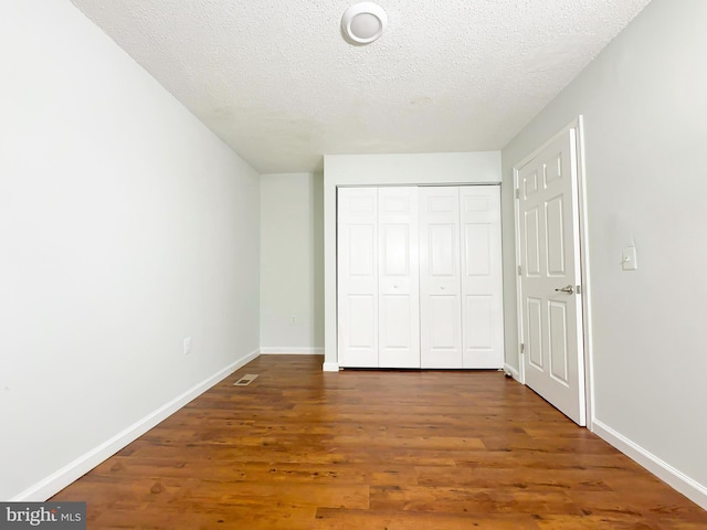 unfurnished bedroom featuring a textured ceiling, a closet, wood finished floors, and baseboards