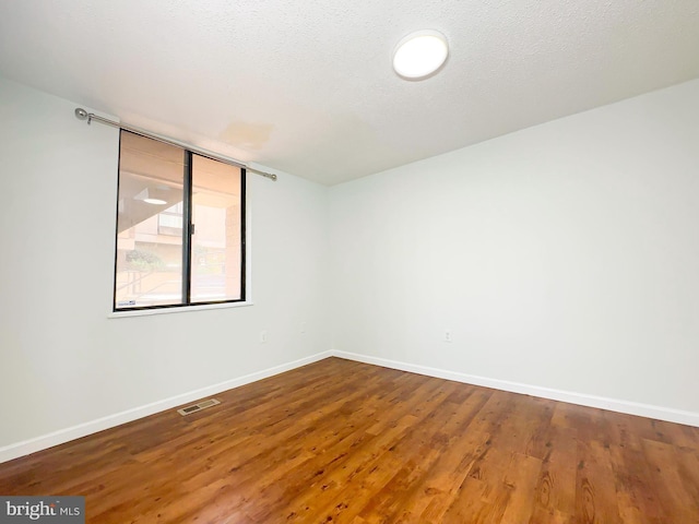 spare room featuring a textured ceiling, wood finished floors, visible vents, and baseboards