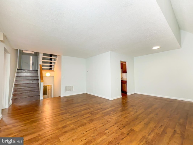 unfurnished living room featuring visible vents, a textured ceiling, wood finished floors, baseboards, and stairs