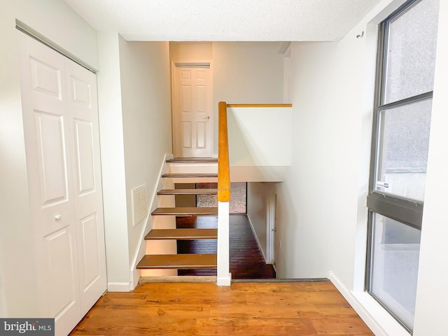 stairs with visible vents, a textured ceiling, baseboards, and wood finished floors