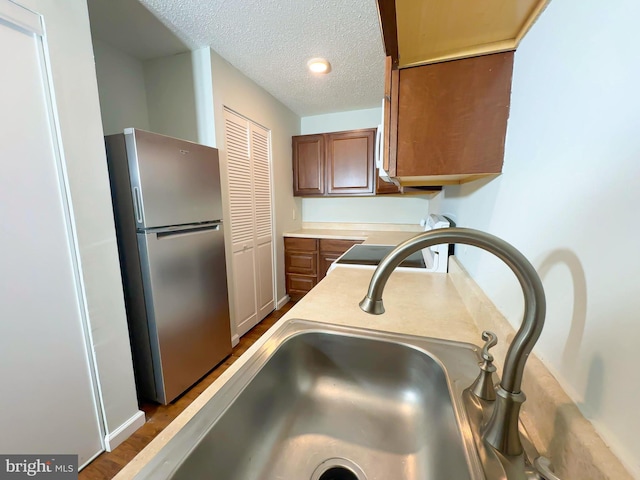 kitchen featuring a textured ceiling, a sink, light countertops, freestanding refrigerator, and brown cabinets