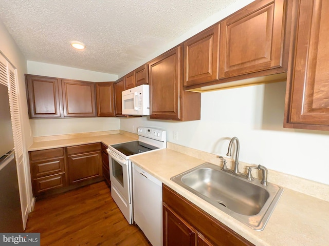 kitchen featuring a textured ceiling, white appliances, a sink, light countertops, and dark wood-style floors