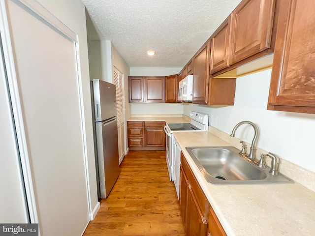 kitchen with a textured ceiling, light wood-style flooring, white appliances, a sink, and light countertops