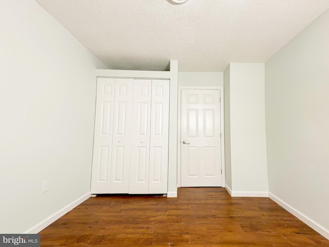 unfurnished bedroom with a textured ceiling, a closet, wood finished floors, and baseboards