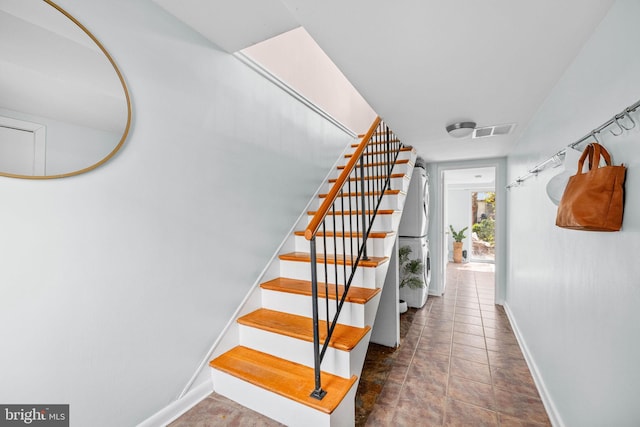 stairway featuring stacked washing maching and dryer, baseboards, and visible vents