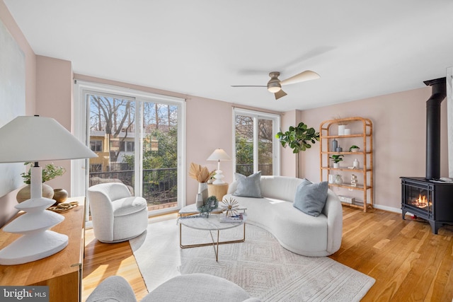 living area featuring a wood stove, light wood-style flooring, baseboards, and ceiling fan