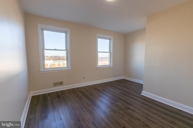 empty room featuring plenty of natural light, visible vents, dark wood finished floors, and baseboards