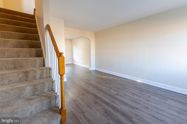 stairway featuring baseboards, arched walkways, and wood finished floors