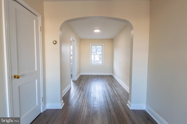 interior space featuring baseboards, arched walkways, and dark wood finished floors