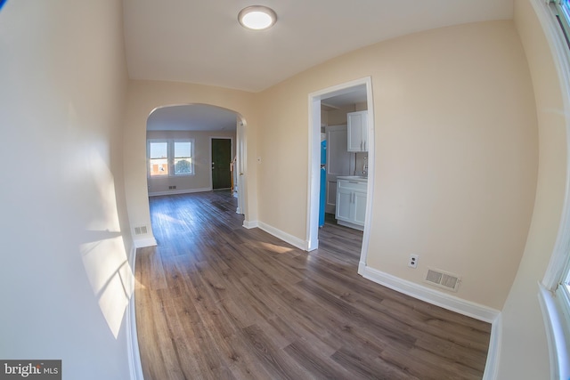 interior space featuring baseboards, visible vents, arched walkways, and dark wood-type flooring