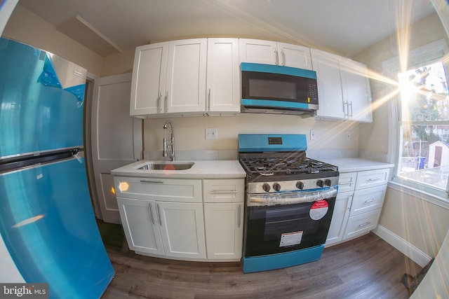 kitchen featuring dark wood finished floors, freestanding refrigerator, stainless steel gas range, white cabinetry, and a sink