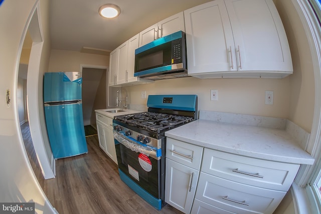 kitchen with dark wood finished floors, appliances with stainless steel finishes, light stone countertops, white cabinetry, and a sink