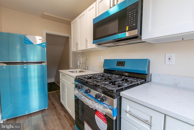 kitchen featuring dark wood-style floors, stainless steel appliances, white cabinets, a sink, and light stone countertops