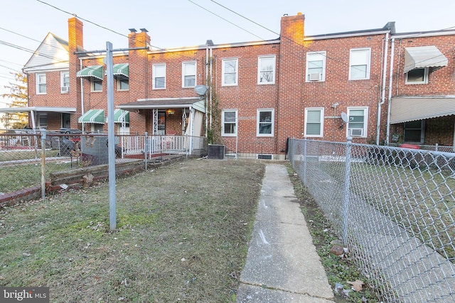 back of house featuring brick siding, a lawn, cooling unit, and fence