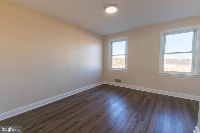 spare room featuring dark wood-style flooring, visible vents, and baseboards