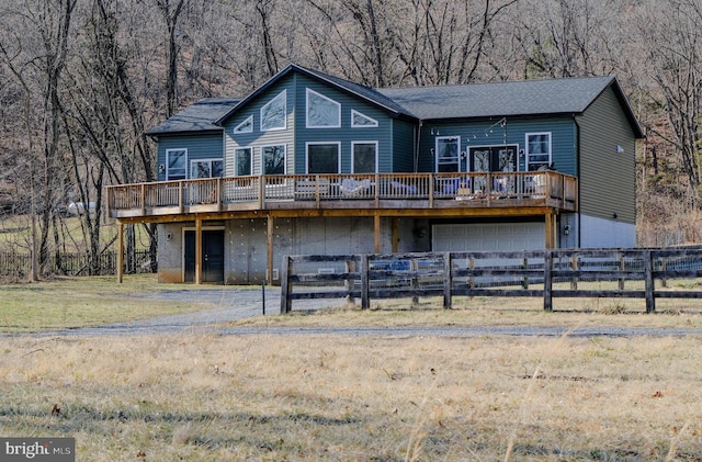 view of front facade with dirt driveway, a wooden deck, fence, a garage, and a front lawn