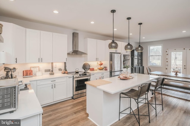 kitchen featuring stainless steel appliances, a breakfast bar, white cabinetry, light countertops, and wall chimney range hood