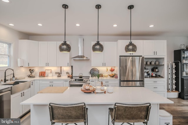 kitchen with a breakfast bar area, stainless steel appliances, white cabinets, a sink, and wall chimney exhaust hood