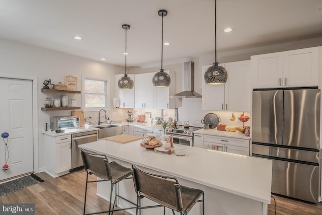 kitchen with white cabinets, appliances with stainless steel finishes, light countertops, wall chimney range hood, and a sink