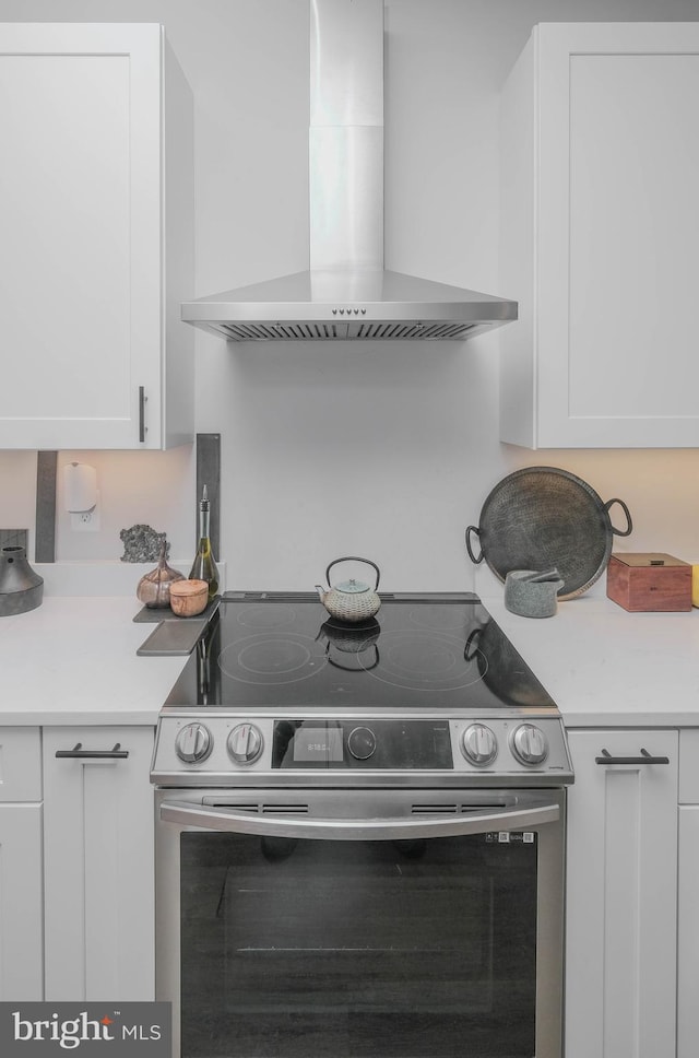 kitchen with light countertops, white cabinets, wall chimney exhaust hood, and stainless steel electric stove