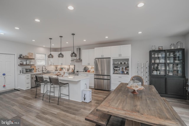 kitchen featuring appliances with stainless steel finishes, a kitchen island, wall chimney range hood, and white cabinetry