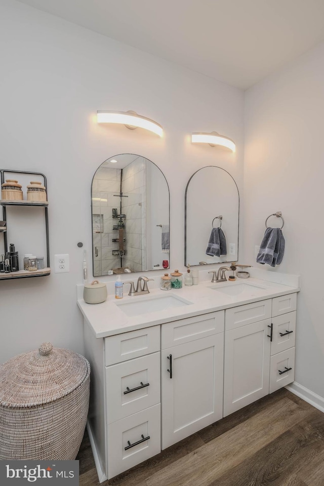 bathroom featuring double vanity, tiled shower, a sink, and wood finished floors