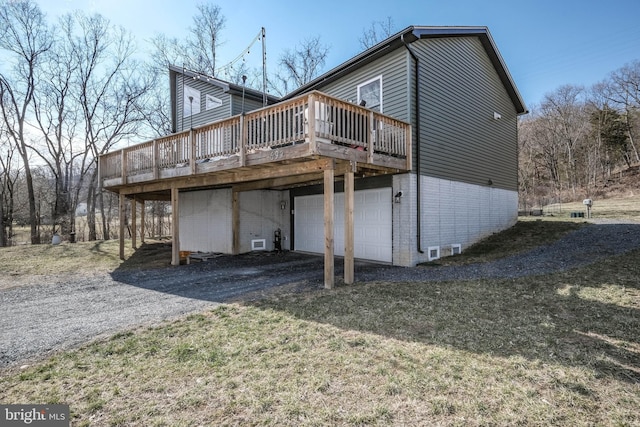 rear view of property featuring a garage, driveway, brick siding, and a wooden deck